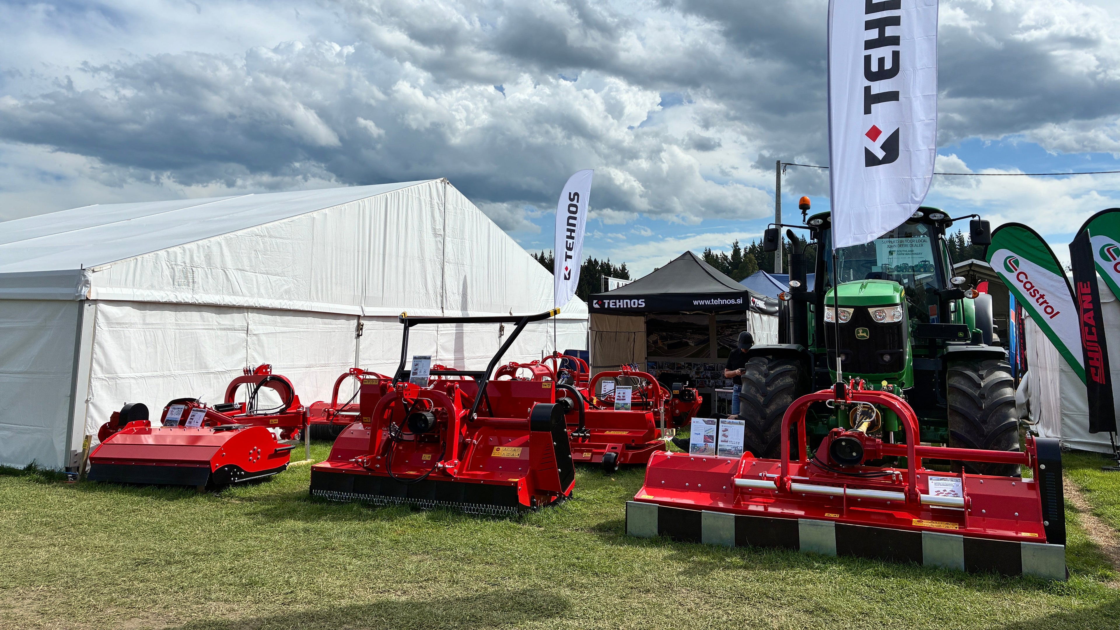 Tractor and agricultural equipment on display with Tehnos branding under a cloudy sky.